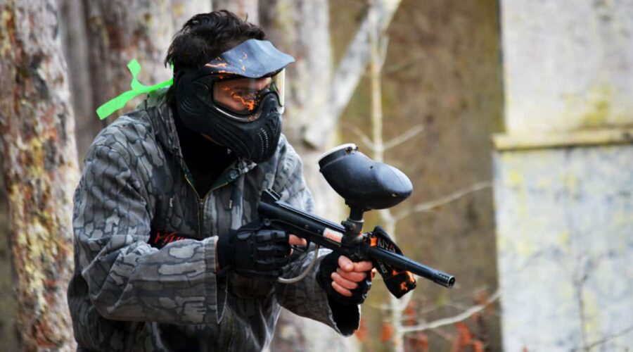 Une personne portant un équipement de protection et un masque tient un pistolet de paintball lors d’une partie de paintball en plein air. Une personne portant un équipement de protection et un masque tient un pistolet de paintball lors d'une partie de paintball en plein air.