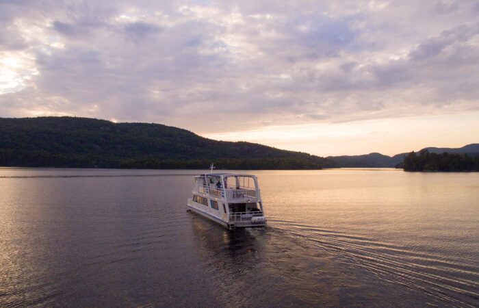 A white boat moves across a calm lake with forested hills and a cloudy sky in the background during sunset. A white boat moves across a calm lake with forested hills and a cloudy sky in the background during sunset.