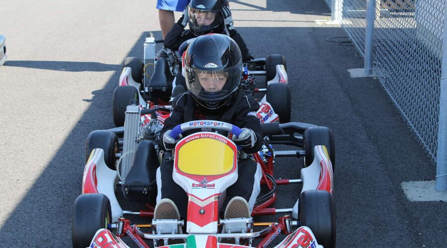 Deux enfants portant des casques sont assis dans des karts sur la piste pour enfants de Go-kart Mont-Tremblant, alignés sur une piste asphaltée et se préparant à faire la course, avec une personne se tenant à proximité. Deux enfants portant des casques sont assis dans des karts sur la piste pour enfants de Go-kart Mont-Tremblant, alignés sur une piste asphaltée et se préparant à faire la course, avec une personne se tenant à proximité.