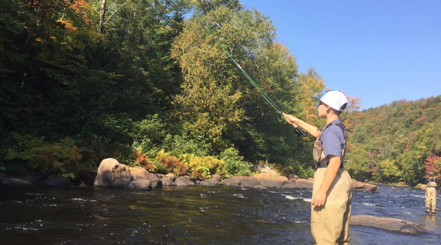 Une personne portant des cuissardes et une casquette se tient dans une rivière, profitant d’une découverte en famille pendant la Pêche à la mouche, entourée d’arbres et de rochers par une journée ensoleillée. Une personne portant des cuissardes et une casquette se tient dans une rivière, profitant d'une découverte en famille pendant la Pêche à la mouche, entourée d'arbres et de rochers par une journée ensoleillée.