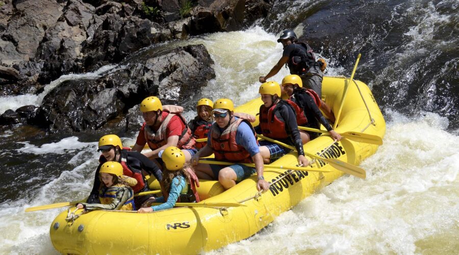 A group of people wearing helmets and life jackets paddle a yellow inflatable raft down a rocky, whitewater river. A group of people wearing helmets and life jackets paddle a yellow inflatable raft down a rocky, whitewater river.