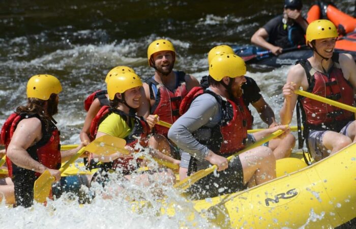 Un groupe de personnes portant des casques jaunes et des gilets de sauvetage rouges pagaient sur un radeau pneumatique jaune dans des rapides d’eau vive exaltants près de Tremblant. Un groupe de personnes portant des casques jaunes et des gilets de sauvetage rouges pagaient sur un radeau pneumatique jaune dans des rapides d'eau vive exaltants près de Tremblant.