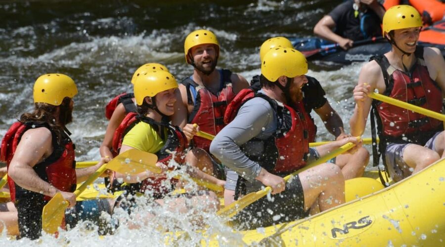 A group of people wearing yellow helmets and red life jackets paddling a yellow inflatable raft through whitewater rapids. A group of people wearing yellow helmets and red life jackets paddling a yellow inflatable raft through whitewater rapids.