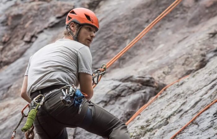 A person wearing a helmet and climbing gear is rock climbing outdoors, secured with ropes against a rocky surface. A person wearing a helmet and climbing gear is rock climbing outdoors, secured with ropes against a rocky surface.