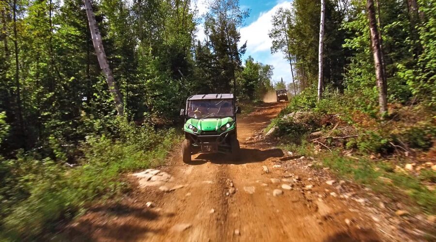 Un véhicule tout-terrain VTT vert roule sur un chemin de terre rocailleux à travers une forêt, avec un autre véhicule visible à l’arrière-plan sous un ciel bleu, idéal pour les randonnées tout-terrain. Un véhicule tout-terrain VTT vert roule sur un chemin de terre rocailleux à travers une forêt, avec un autre véhicule visible à l'arrière-plan sous un ciel bleu, idéal pour les randonnées tout-terrain.