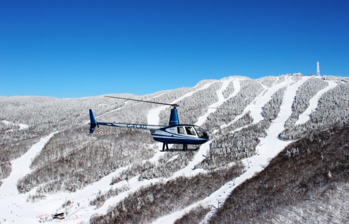 A blue and white helicopter flies over a snow-covered mountain with ski slopes, offering breathtaking scenic flights under a clear blue sky. A blue and white helicopter flies over a snow-covered mountain with ski slopes, offering breathtaking scenic flights under a clear blue sky.