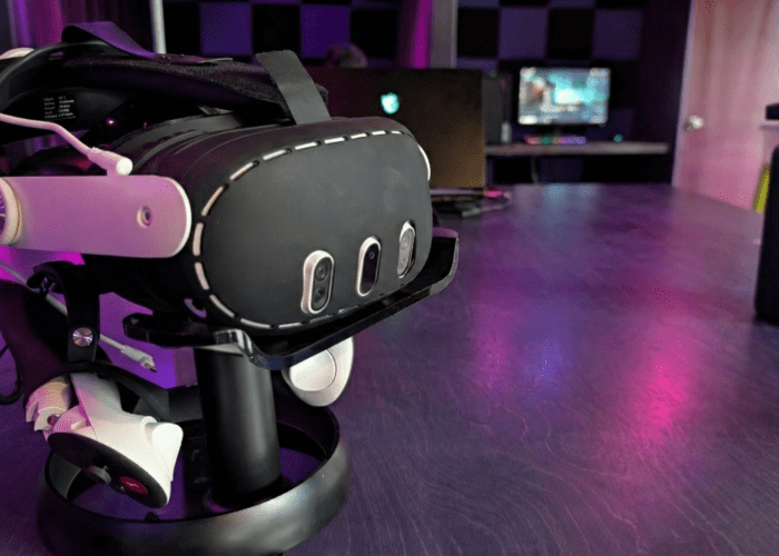 A VR headset and controllers rest on a stand on a blue table, hinting at an immersive Arcade VR experience; a water bottle and computer setup are visible in the background, perfect for those considering headset rental.