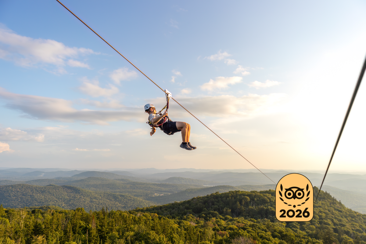 Person ziplining over the forested mountain landscape of Mont-Tremblant under a blue sky, with a "2026" badge in the lower right corner.