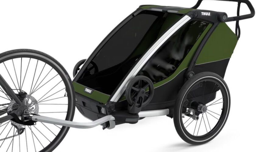A green and black Thule bike trailer with two wheels is attached to a bicycle, designed for carrying children or cargo.