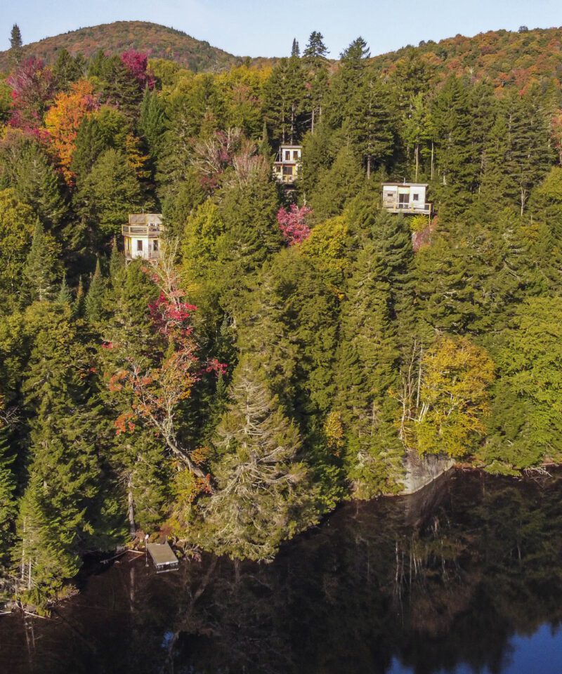 Houses are partially visible among dense, colorful autumn trees on a hillside above a dark, calm lake.