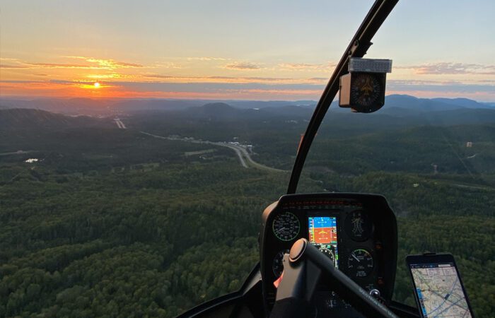 Faites l'expérience d'un Vol au sommet à l'intérieur d'un cockpit Hélicoptère, survolant un paysage forestier au coucher du soleil avec les écrans de navigation et les commandes à portée de vue.