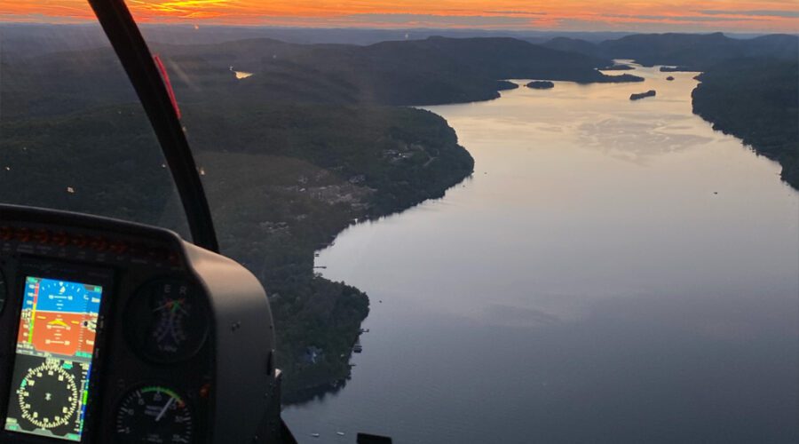 A breathtaking view from inside a helicopter cockpit at sunset, overlooking a winding river as illuminated flight instruments guide the way toward the distant summit.